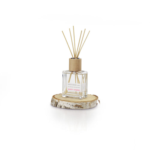 A minimalist square glass bottle with a wooden cap holds reed sticks, infused with essential oils for the Sweet Grapefruit Diffuser fragrance. This 