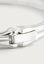 Load image into Gallery viewer, Close-up of the Bamboo Hinged Bangle - Silver, crafted from sterling silver-dipped brass. This sleek bracelet features a secure clasp with small crystals for subtle sparkle, set against a smooth and reflective surface with gentle curves against a soft, neutral gray background.
