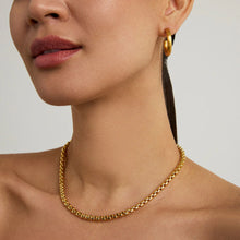 Load image into Gallery viewer, With smooth skin and natural makeup highlighting soft pink lips, they wear a Tokyo Chain Necklace and gold hoop earring. Their hair is pulled back in a plain, light-colored background, emphasizing the jewelry and neckline.
