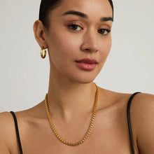 Load image into Gallery viewer, A person with dark hair pulled back, wearing a simple black strap outfit, gold hoop earrings, and a Tokyo Chain Necklace. Their calm, focused expression is accentuated by the plain light background. The overall look is elegant and minimalistic.
