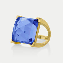 Load image into Gallery viewer, Meet the Plaza Ring: a gold band featuring a wide, smooth finish and adorned with a square-cut blue gemstone. The hand-faceted masterpiece reflects light brilliantly, its vivid color set against a light gray background.
