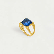 Load image into Gallery viewer, The Mini Plaza Ring showcases a stunning square-cut blue gemstone on a split shank. With a hand-faceted gem and smooth gold band, it exudes an elegant, modern yet classic charm against a plain white background.
