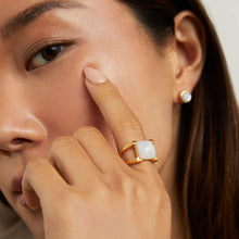 Load image into Gallery viewer, A close-up shows a person touching their face with the Mini Plaza Ring, which showcases a square-shaped, hand-faceted gemstone. Their look is complemented by a small round pearl earring. Soft lighting accentuates their smooth skin and dark brown hair, highlighting each jewelry detail.
