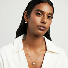 Load image into Gallery viewer, A woman with long dark hair poses against a light gray background, wearing gold earrings and the Signature Pendant made from man-made gemstones, paired with a white shirt. Her expression is neutral.
