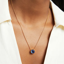 Load image into Gallery viewer, Close-up of a person wearing the Signature Pendant featuring a round blue man-made gemstone. They are dressed in a light beige collared shirt, slightly open at the neck, emphasizing the pendant&#39;s elegant simplicity against their skin.
