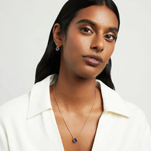 Load image into Gallery viewer, A woman with long black hair wears a white open-collar shirt and a gold Signature Pendant necklace. Her matching earrings, adorned with dazzling blue gemstones, compose an elegant ensemble. The plain white background highlights her poised expression and sophisticated jewelry.
