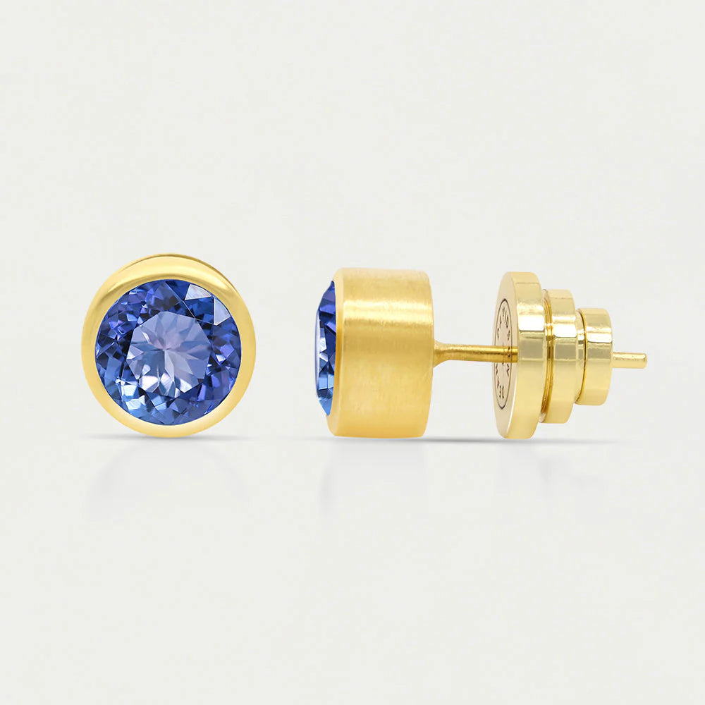 Two gold Signature Midi Studs showcase circular man-made blue gemstones. One earring is presented from the front, highlighting the sparkling stone, while the other reveals Dean Davidson's elegant gold setting and post with a butterfly clutch against a plain white background.