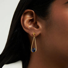 Load image into Gallery viewer, A person wears the Mini Ipanema Earrings featuring a gold teardrop with a dark blue, checkered-cut gemstone and a small gold stud. Their dark hair contrasts with their white top against a neutral background.
