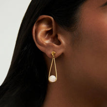 Load image into Gallery viewer, The Mini Ipanema Earrings feature a gold teardrop with ethically sourced, checkered-cut gemstones and a dangling white round stone from a delicate stud, subtly complementing the model&#39;s smooth skin and dark hair in the background.
