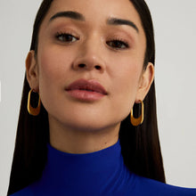 Load image into Gallery viewer, With long dark hair, a person in a blue turtleneck wears Crosby Hinged Hoops. The light-colored background highlights their serene expression and adds a modern edge by contrasting the bright clothing with the elegant earrings.
