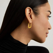 Load image into Gallery viewer, A side profile of a person with long, black hair, wearing a black turtleneck showcases them adorned with Crosby Hinged Huggie Hoops. The neutral background accentuates their subtle makeup and the earrings&#39; shine.
