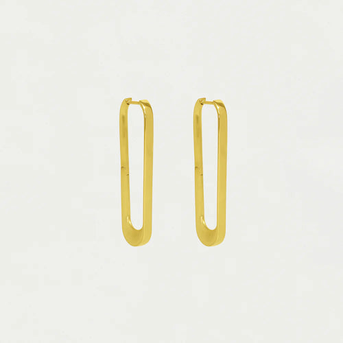 The Crosby Drop Hoops, crafted from 18kt gold, hang elegantly with a sleek, minimalistic design. Inspired by New York architecture, these elongated earrings feature rounded corners and a polished finish that casts subtle shadows against a plain background.