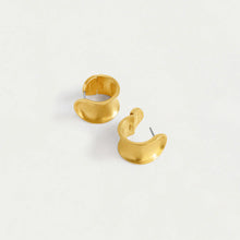 Load image into Gallery viewer, The Sol Huggie Hoops, a pair of gold crescent-shaped earrings, are showcased on a light cream background. Each hypoallergenic earring features a smooth, shiny finish with subtle curves for a minimalist and elegant look. The visible fastening posts highlight their circular, open-loop design.
