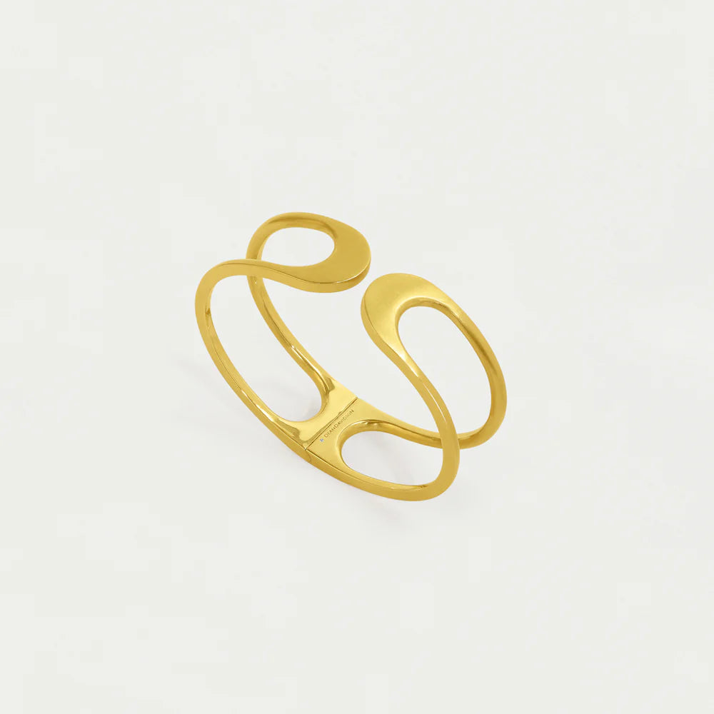 The Crosby Midi Cuff features a 22-Karat gold finish with an abstract, interlocking design. Its band forms elegant curving loops, gleaming like polished metal against a plain white background to accentuate its artistic shape.