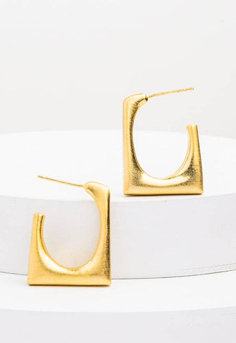 The Geometric Hoops in Gold, crafted with 14K plated gold, are elegantly showcased upright on stacked white cylindrical platforms. Featuring smooth, polished surfaces and slender posts for fastening, these modern earrings exude elegance against a soft, neutral white background.