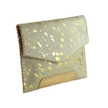 Load image into Gallery viewer, The Diana Clutch - Cowhide Hairon Leather is a small, rectangular envelope-style purse crafted from cowhide hairon leather adorned with gold speckles. It features a flap closure and whipstitch detailing along the edges for an artisanal touch, with a pale cream color complemented by prominent golden accents.
