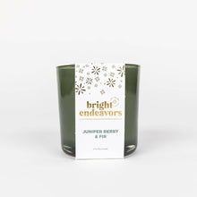 Load image into Gallery viewer, A clean and minimalist candle holder with a &quot;bright endeavors&quot; label in gold and navy text showcases a green glass design crafted from recycled materials. The white background of the label features small gold stars and dots, while the text reads &quot;Juniper Berry &amp; Fir, 7 oz Soy Candle.
