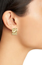 Load image into Gallery viewer, Close-up of a person wearing a Textured Elongated Clip-On Earring crafted from 24 kt gold on their ear. The hammered surface beautifully reflects light. Their smooth skin and pulled-back dark hair showcase the earring&#39;s size and detail against a light background.
