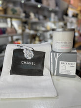 Load image into Gallery viewer, A display showcases the Great Girlfriend Gift Set with a white guest towel featuring a black square and &quot;Chanel&quot; under a rose illustration, beside a gray Birch House Candles box and grapefruit-scented white soy candle. Shelves with various items softly blur in the background.
