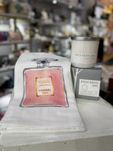 Load image into Gallery viewer, The Great Girlfriend Gift Set features a guest towel with a pink Chanel No. 5 perfume bottle design, complemented by two Birch House soy candles labeled &quot;All Natural Soy Wax&quot; and &quot;Scented in Sweet Grapefruit,&quot; set against blurred store shelves.
