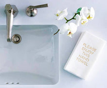 Load image into Gallery viewer, In a bathroom scene, a sleek faucet and sink sit on a white countertop. A white guest towel with gold foil reading &quot;PLEASE ENJOY THIS HAND TOWEL,&quot; from the Cloth-Like Guest Towels - Year Round Themes, is nearby. Blooming white orchids above add elegance.
