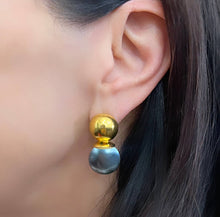 Load image into Gallery viewer, A close-up captures a woman&#39;s ear accessorized with the exquisite Gold Lady Earrings. The gold domed top sparkles brilliantly, complementing the bottom section&#39;s flat, round metallic disc adorned with a reflective silver finish. Her dark, straight hair partially veils her ear, creating an enigmatic allure.
