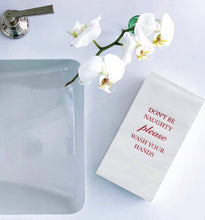 Load image into Gallery viewer, A bathroom sink with a white orchid features a beige guest towel from the Cloth-Like Guest Towels - Year Round Themes line. The towel is foil-embossed with red text reading, &quot;DON&#39;T BE NAUGHTY please WASH YOUR HANDS,&quot; and sits neatly folded next to the silver faucet.
