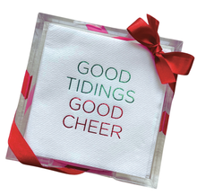 Load image into Gallery viewer, The Cocktail Napkin Acrylic Tray Set - Year Round Entertaining includes a clear acrylic tray that stores disposable white napkins featuring &quot;GOOD TIDINGS GOOD CHEER&quot; in gradient green and red text. Wrapped with a red ribbon tied into a bow at the corner, this set makes an ideal hostess gift with its festive appearance.
