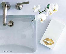 Load image into Gallery viewer, A white bathroom sink with a silver faucet sits beside a white orchid stem. A stack of Cloth-Like Guest Towels - Year Round Themes featuring a gold lips print adorns the countertop, against a pristine white background for an elegant and minimalist look.
