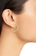 Load image into Gallery viewer, Close-up of a person wearing Small Overlap Hoop Earrings on their left ear. These gold-plated earrings have a medium size with a smooth texture. The person&#39;s skin appears smooth, and their dark hair is tucked behind the ear, accentuating the earring along with parts of the neck and cheek against a white background.
