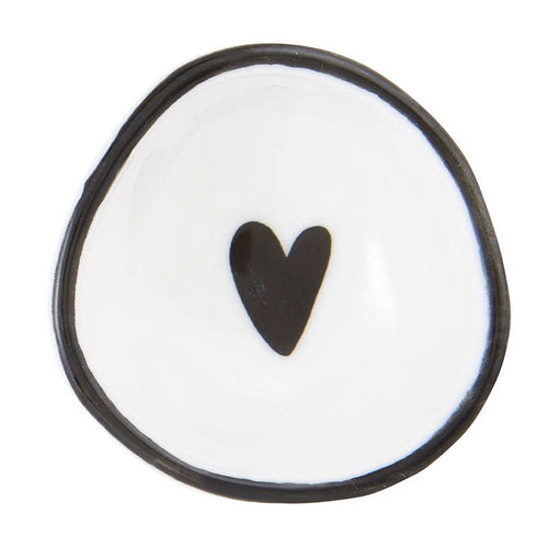 The Ring Dish is a small, white ceramic piece with a slightly irregular round shape, featuring a black heart in the center and a black rim. Its glossy finish adds to its elegant handmade look, perfect for storing rings.