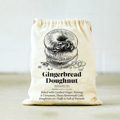 The Gingerbread Doughnut Baking Mix & Mold Set includes a beige drawstring bag adorned with an illustration of stacked doughnuts and marked 