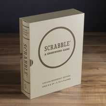 Load image into Gallery viewer, A beige Scrabble Vintage Bookshelf Edition box, styled like a book, stands upright on a wooden surface with minimalist brown lettering displaying &quot;SCRABBLE: A CROSSWORD GAME&quot; on the front. This edition features premium game components and is designed for ages 8 and up, accommodating 2 to 4 players.
