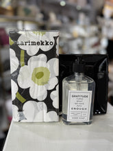 Load image into Gallery viewer, A bottle of Gratitude Hand Soap with a label that reads, &quot;GRATITUDE turns what we have into ENOUGH,&quot; is placed next to Marimekko tissues featuring a bold floral black, white, and green design on a light-colored surface. This creates the inviting atmosphere of a Hand Towel Gift Set against a blurred store backdrop.
