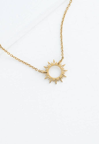 The Mallory Necklace is a hypoallergenic accessory that showcases a gold-plated pendant resembling the sun, with its circular center and pointed rays, set against a light, textured surface. The intricate design and simple yet elegant chain emphasize the pendant's ornate beauty perfectly.