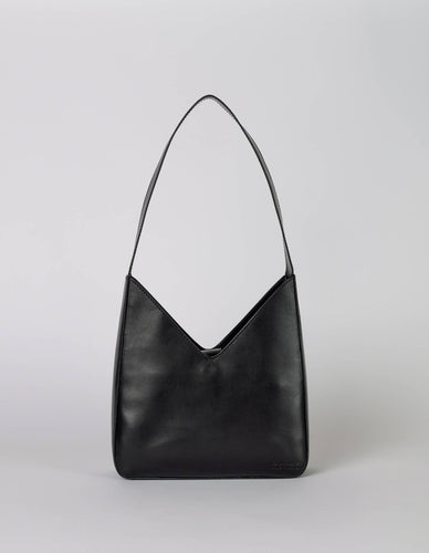 Introducing the Vicky Bag - Classic Leather: a sophisticated black shoulder bag with a minimalist and vintage geometric design. Made from eco-friendly leather, it features a singular strap and distinct triangular shape enhanced by its smooth, glossy finish. The plain light grey background accentuates the bag's elegant and contemporary style.