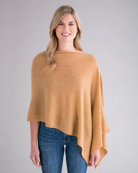 A person with long, blonde hair smiles while wearing the Cashmere Poncho in light brown over blue jeans. The plain, light gray background accentuates the simplicity and elegance of this versatile dress topper.