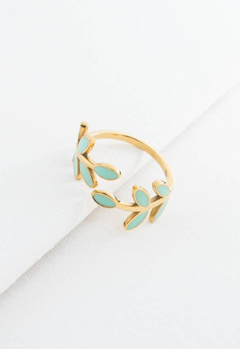 The Seeds of Hope Ring, crafted with a 14K gold plating, showcases a delicate leafy design enhanced by turquoise enamel accents. This adjustable piece is elegantly displayed on a textured white backdrop, emphasizing its minimalist and graceful aesthetic.