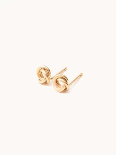 The Evermore Studs feature two gold-filled earrings displayed against a plain white background, each showcasing an intricate love knot design that symbolizes unity and elegance. The polished finish provides a shiny appearance, and the earrings are positioned side by side with their posts visible.