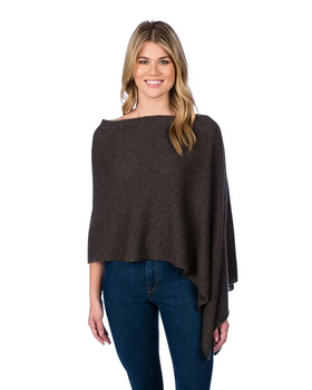 A woman with long blond hair is smiling, wearing the Cashmere Poncho, which is dark gray and features an asymmetrical design. It has a soft, draped appearance as she stands against a plain white background over her blue jeans.