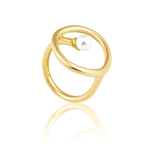 Introducing the Krista Pearl Ring: a distinctive piece showcasing two interlocking circular bands plated in 18K gold, elegantly cradling a single white pearl within the top circle. Designed for durability, it is resistant to water and tarnish, while its reflective surface emits a gentle glow against a white background.