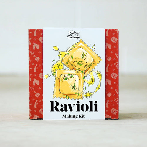 A Ravioli Making Kit comes in a rectangular box, its red sides adorned with pasta-themed illustrations. The front showcases two herb-garnished ravioli drizzled with oil, enticing you to craft fresh pasta filled with homemade ricotta. The 