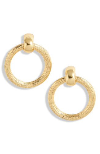 The Large Door Knocker Stud Earrings are showcased against a white background, featuring two hoop earrings plated in 24-kt gold. Each earring boasts a textured, circular ring that dangles gracefully from a smooth, rounded gold stud. The design is simple yet elegant, with a polished finish that beautifully reflects light and is nickel-free.