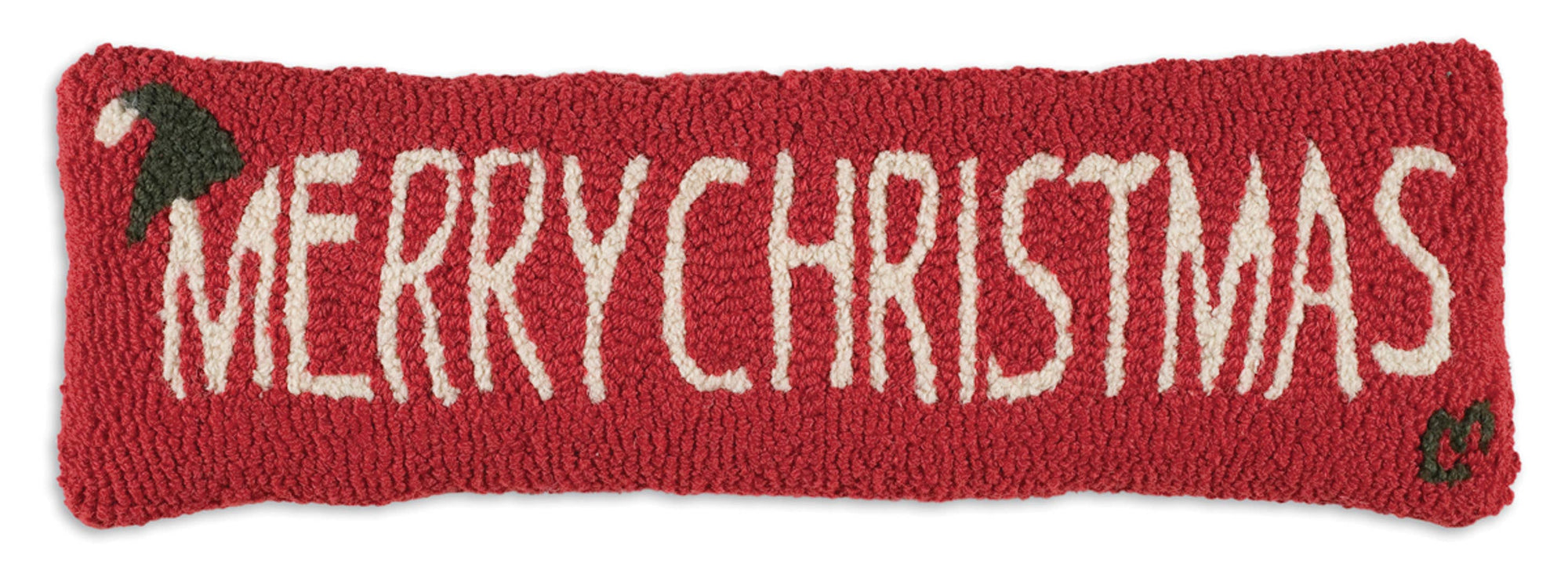 The Merry Christmas Pillow is a handcrafted rectangular piece from India, featuring white hand-stitched text reading "Merry Christmas" on a red background. Each corner showcases a charming design of small green holly leaves with red berries. Made from natural wool, it boasts a knitted or crocheted texture.
